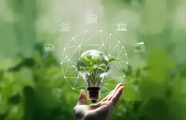 A hand holding a light bulb with a plant inside
