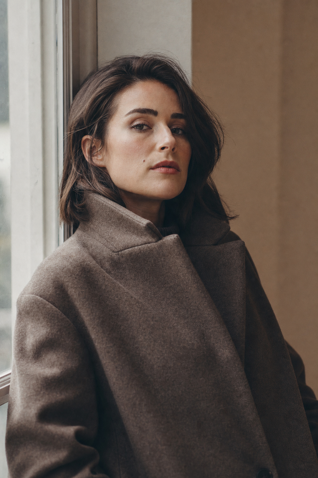 editorial portrait of a woman in a tailored wool coat, soft window light, muted warm tones, shot on 85mm film
