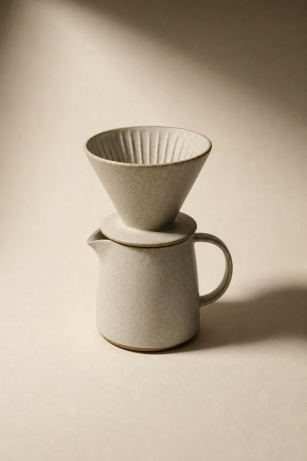 minimalist product shot of a ceramic pour-over coffee maker on warm bone paper, single overhead light, editorial