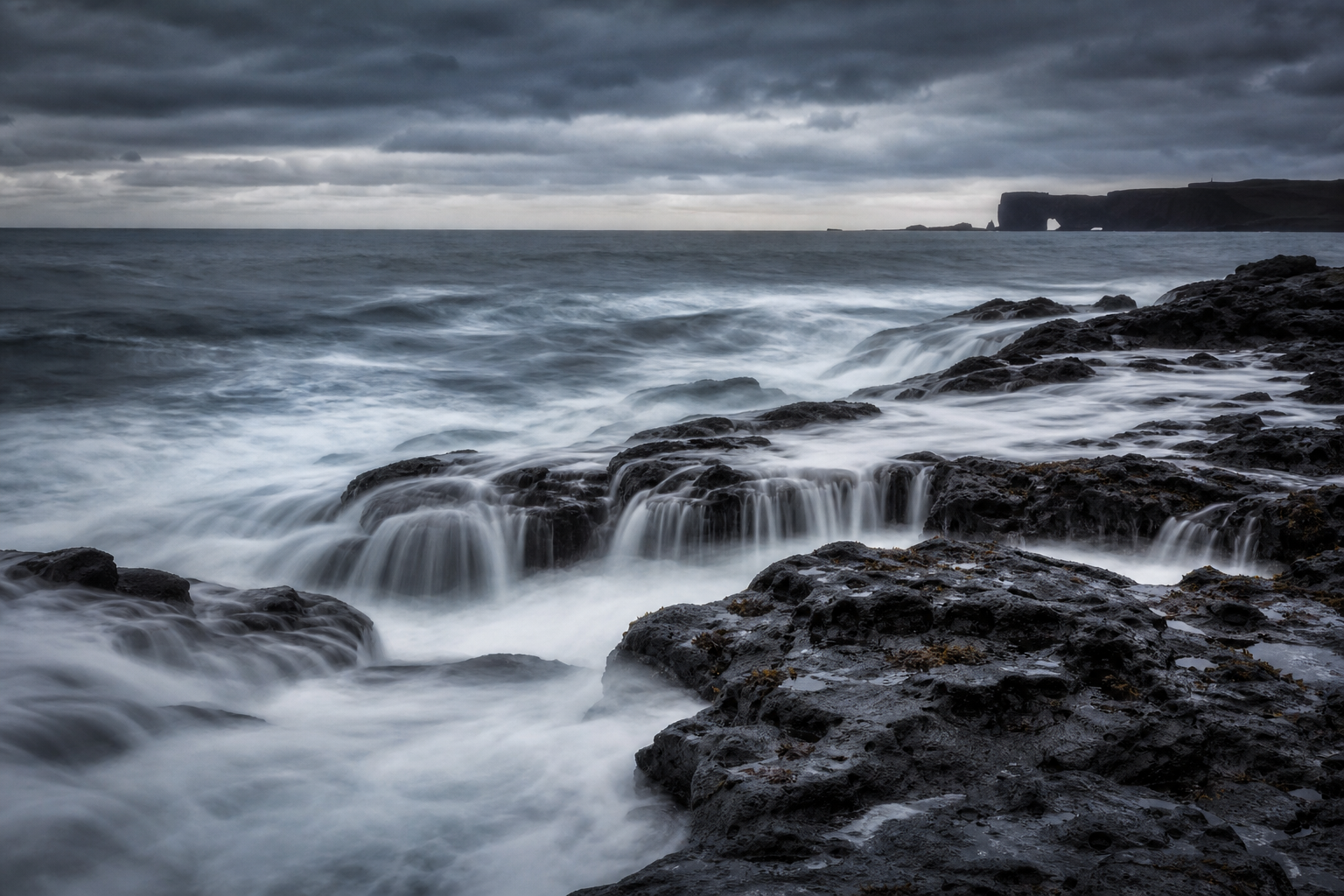 long exposure of ocean waves crashing on black volcanic rocks, silky water, moody overcast sky