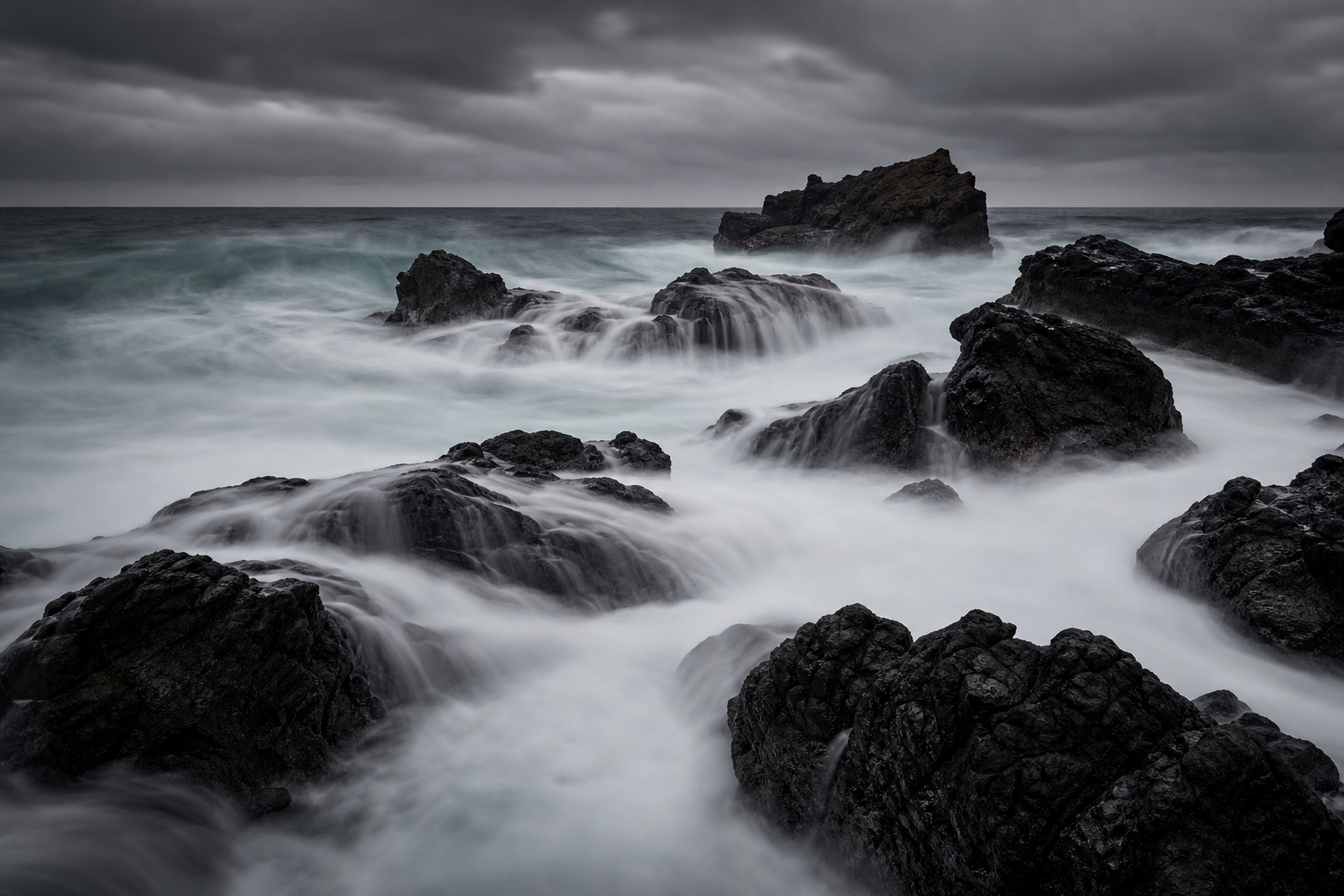 long exposure of ocean waves crashing on black volcanic rocks, silky water, moody overcast sky