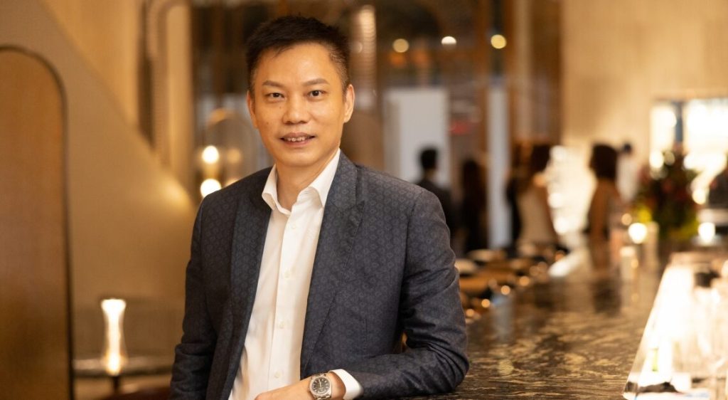 A Wellness Holdings' Arich Tan in a stylish suit at a modern venue, discussing AI-driven hair care solutions by DrScalp.