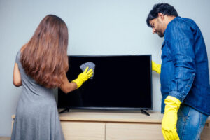 A young couple cleaning a flat TV screen