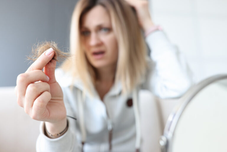 A frustrated woman holds hair in her hand representing signs of balding