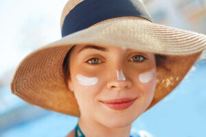 A woman wearing a hat and applying sunscreen for a sun protection