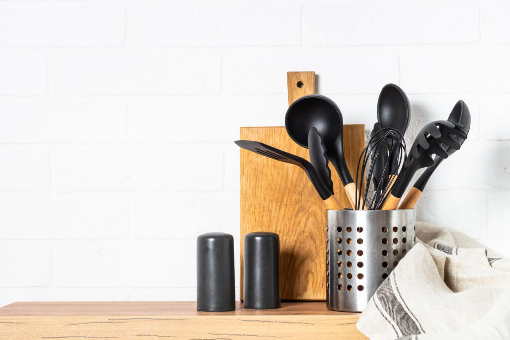 kitchen utensils cooking tools container with wooden cutting board near white wall