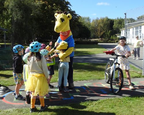 Students dressed in yellow hug Harold the giraffe mascot