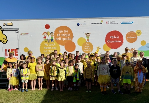 Students and teachers dressed in yellow outside Life Education mobile classroom
