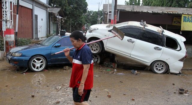 Warga berjalan di dekat tumpukan mobil yang rusak pasca banjir di kawasan Perumahan Pondok Gede Permai Bekasi, Jawa Barat, Kamis (2/1/2020). Arus banjir yang deras telah menyeret mobil-mobil milik warga, lalu tertumpuk di depan pintu masuk perumahan. (istimewa)