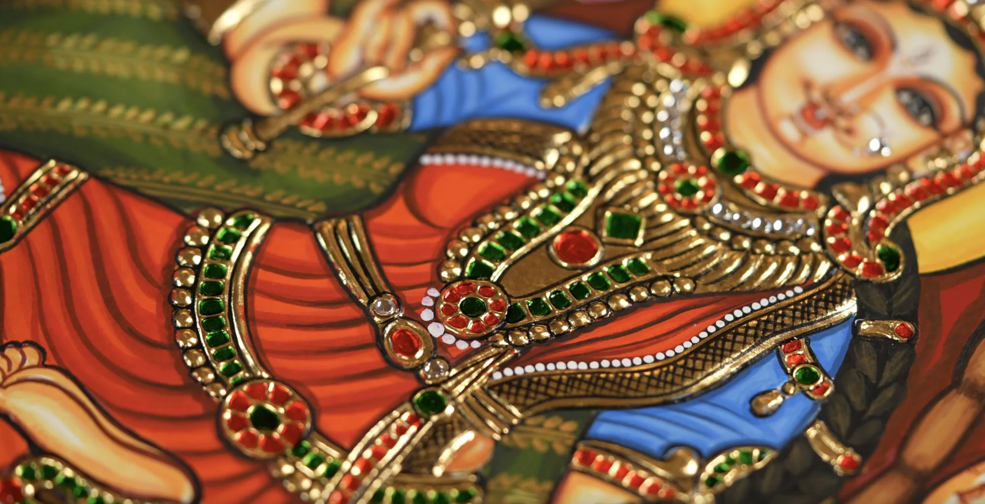 Close-up of gold relief, kundan stones and painted detail on a Tanjore deity