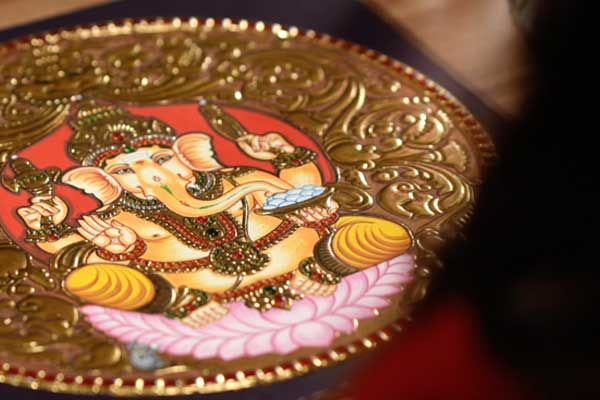 Finishing touches on a round Lord Ganesha Tanjore painting with gold relief