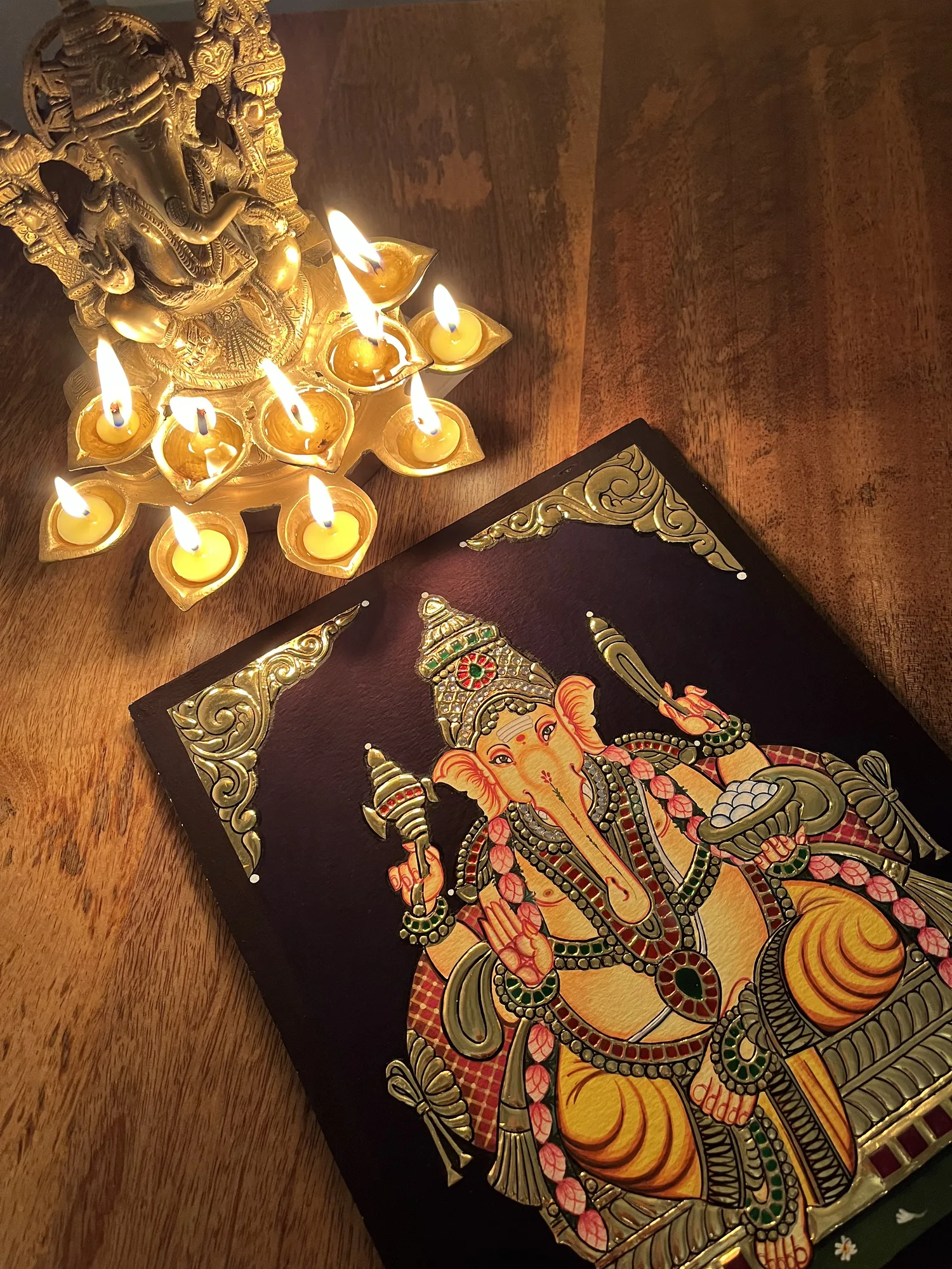 A Lord Ganesha Tanjore painting beside lit oil lamps, styled for a festival