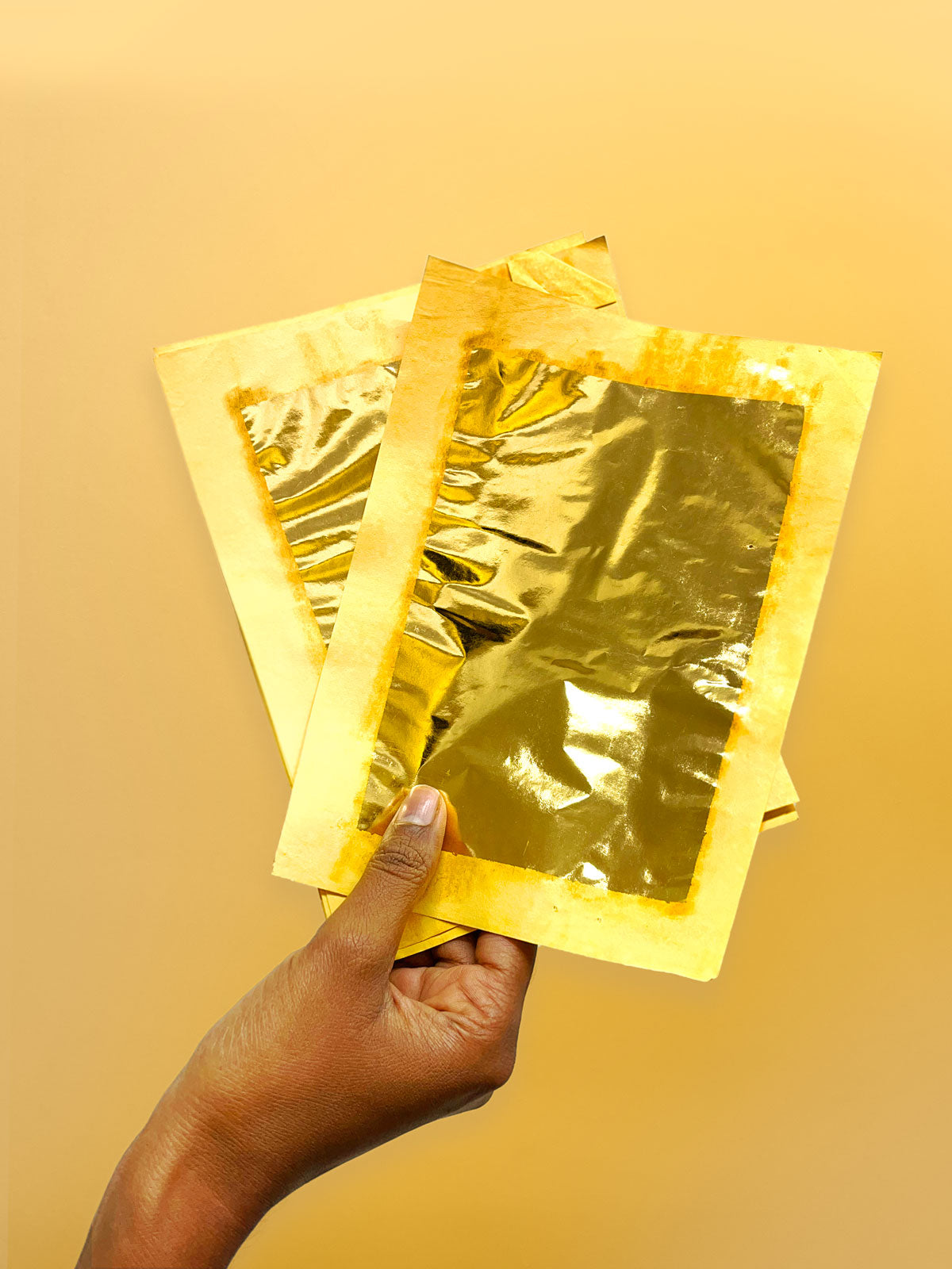 A hand holding sheets of 24 karat gold foil for Tanjore painting