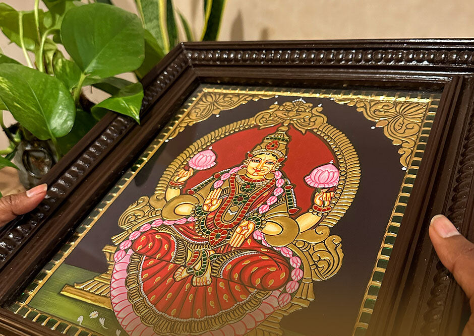 Hands holding a framed Goddess Lakshmi Tanjore painting
