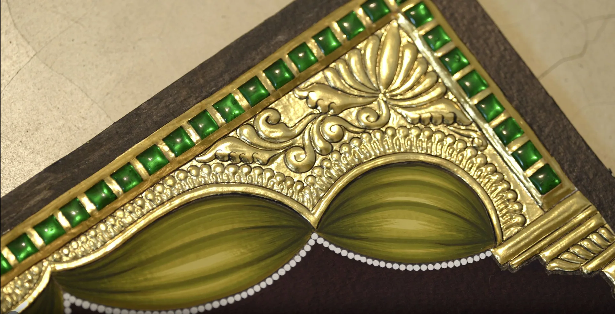 A finished gold Tanjore painting corner with a border of green kundan stones
