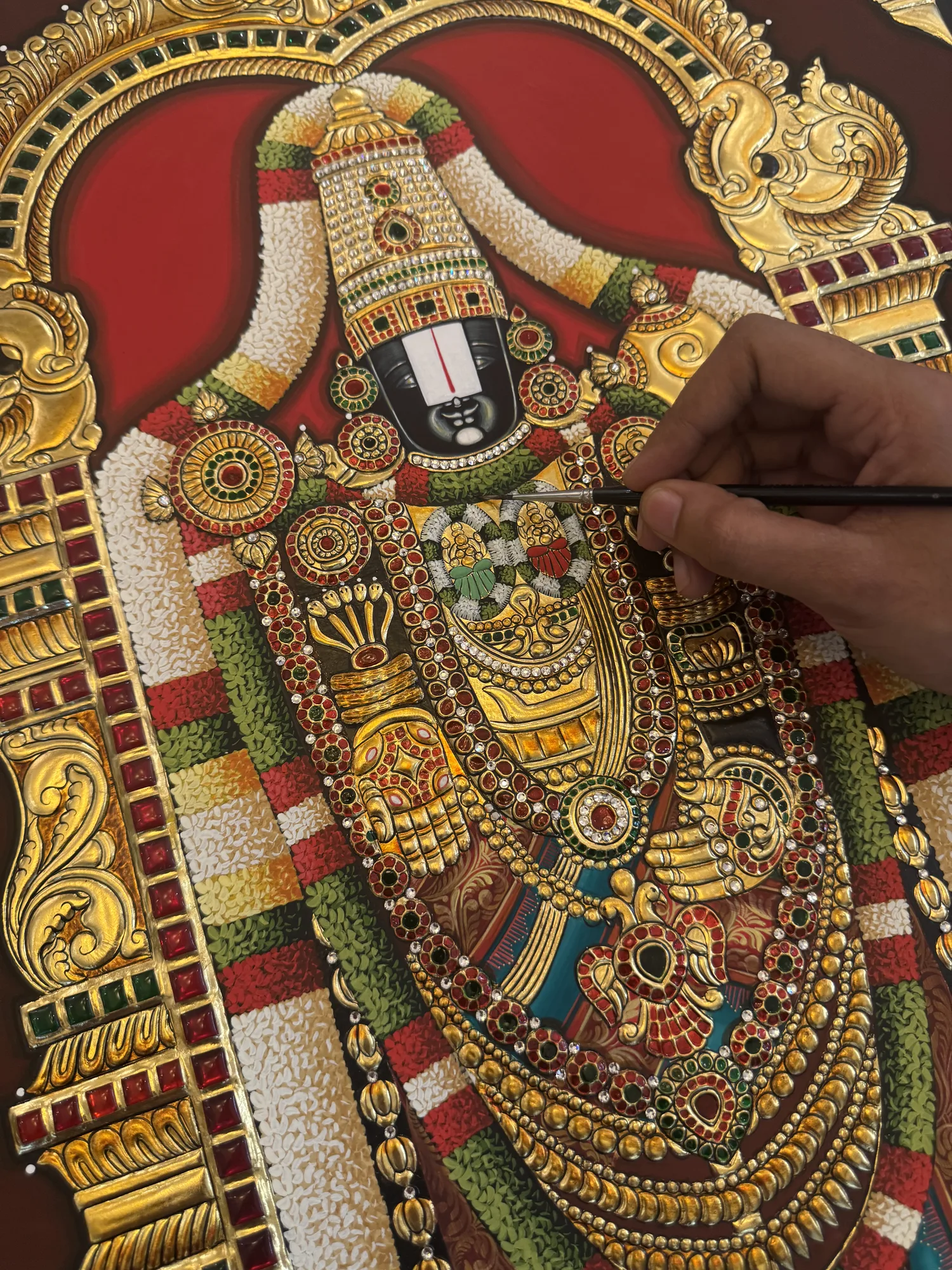 An artist painting fine detail on a Lord Balaji Tanjore painting