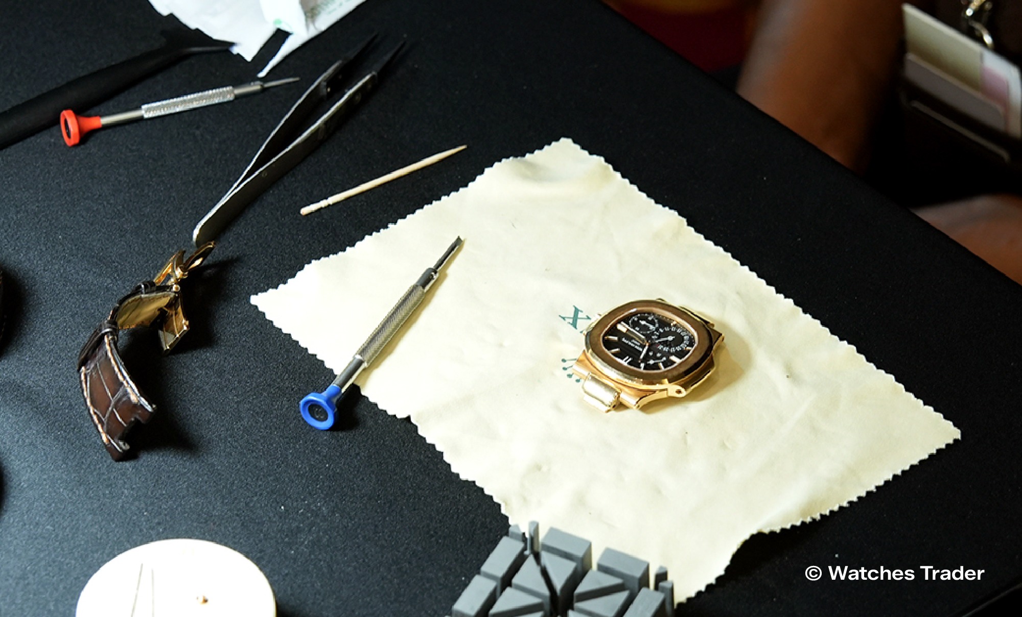 Meja kerja jam tangan dengan Patek Philippe Nautilus rose gold, obeng, pinset, dan strap kulit
