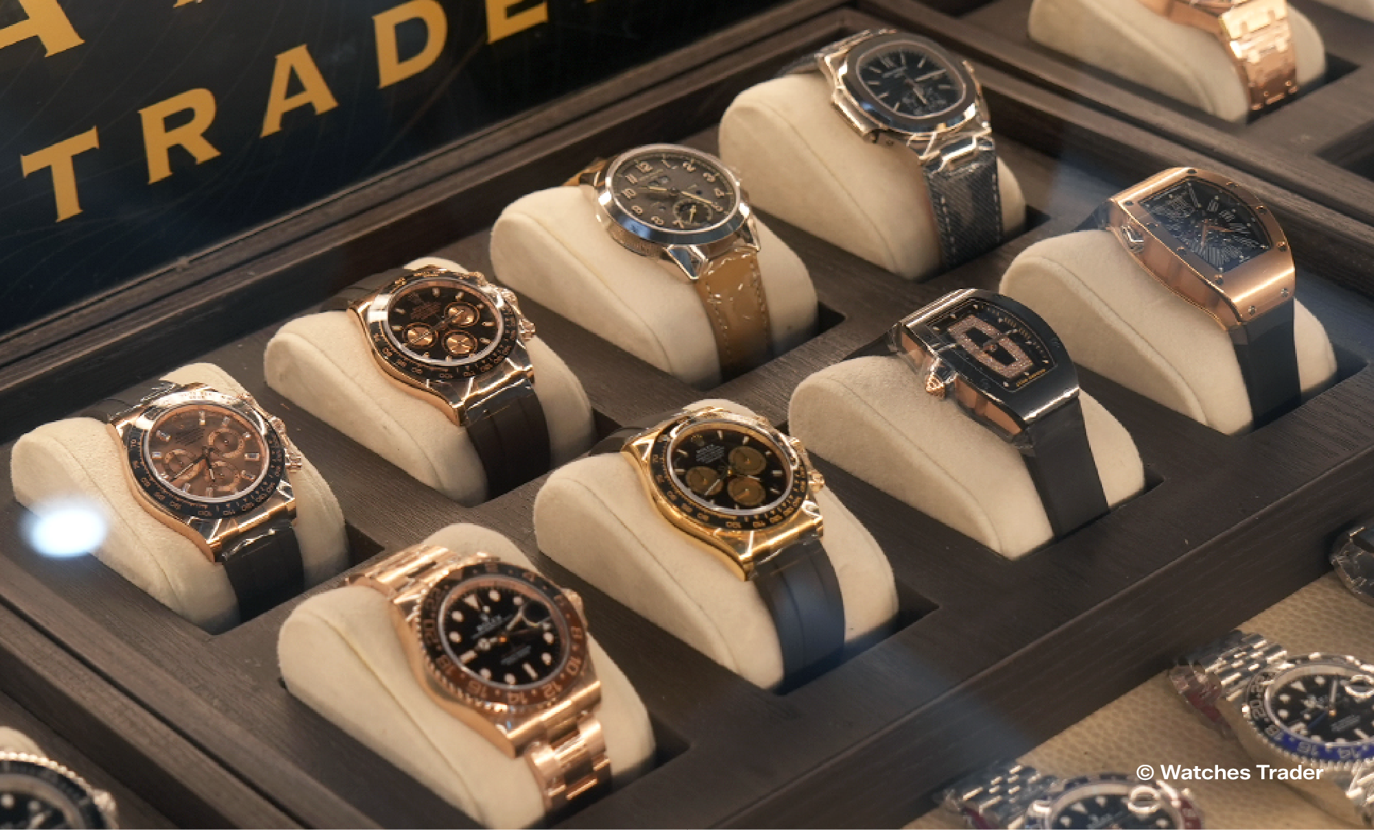 Deretan jam tangan mewah dengan case rose gold dan emas pada bantalan krem di dalam etalase Watches Trader, termasuk model chronograph, tonneau, dan jam dengan bracelet
