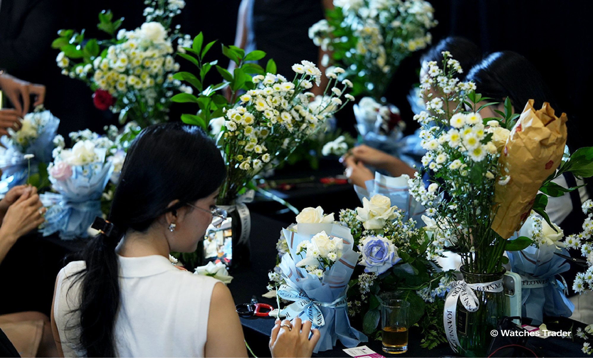 Peserta merangkai buket bunga putih dan biru di meja hitam dalam aktivitas flower bouquet workshop saat acara Watches Trader Journey