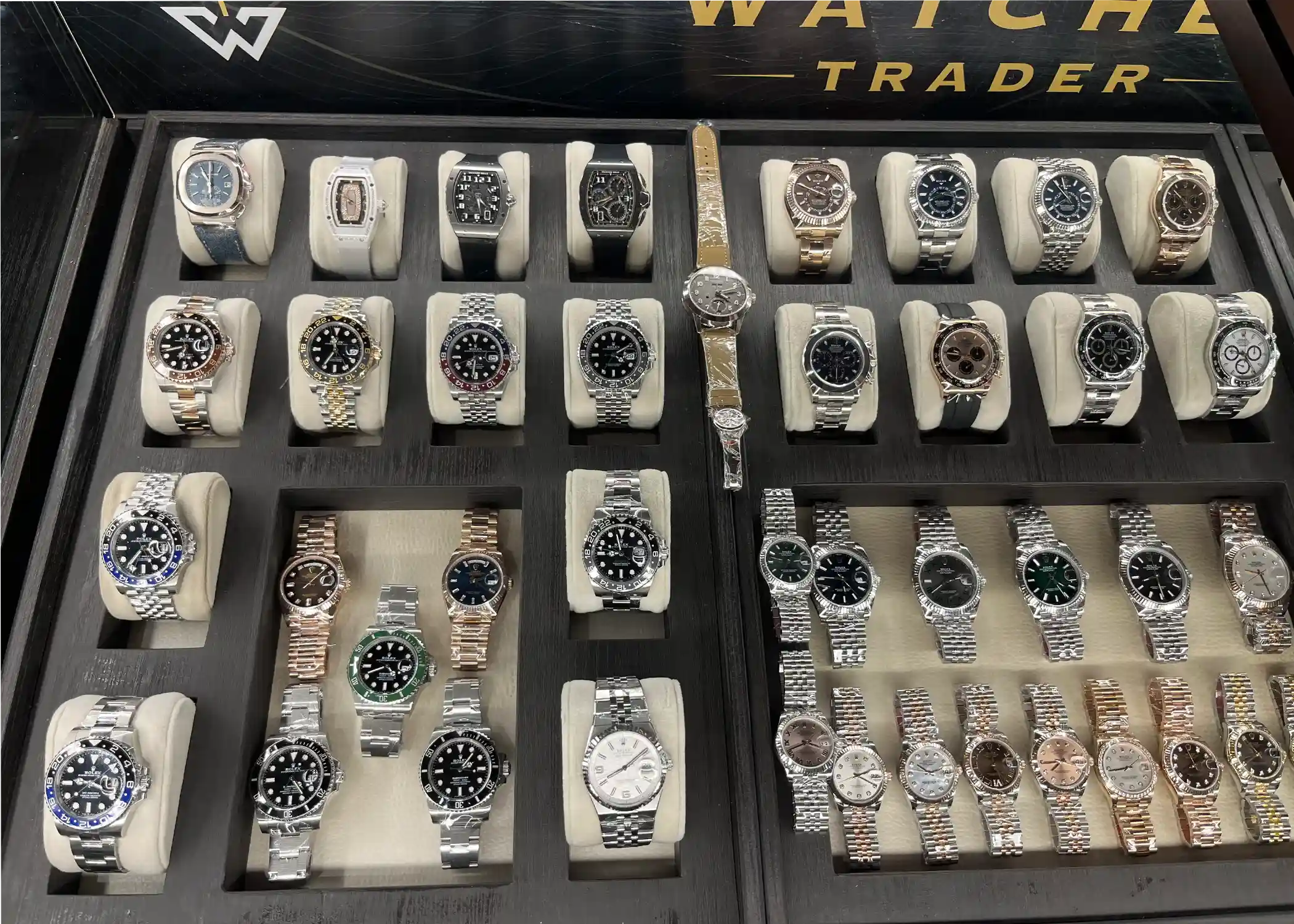Etalase Watches Trader berisi deretan jam tangan mewah, termasuk Rolex GMT-Master II, Daytona, Submariner, dan Datejust, serta Patek Philippe Nautilus dan Richard Mille