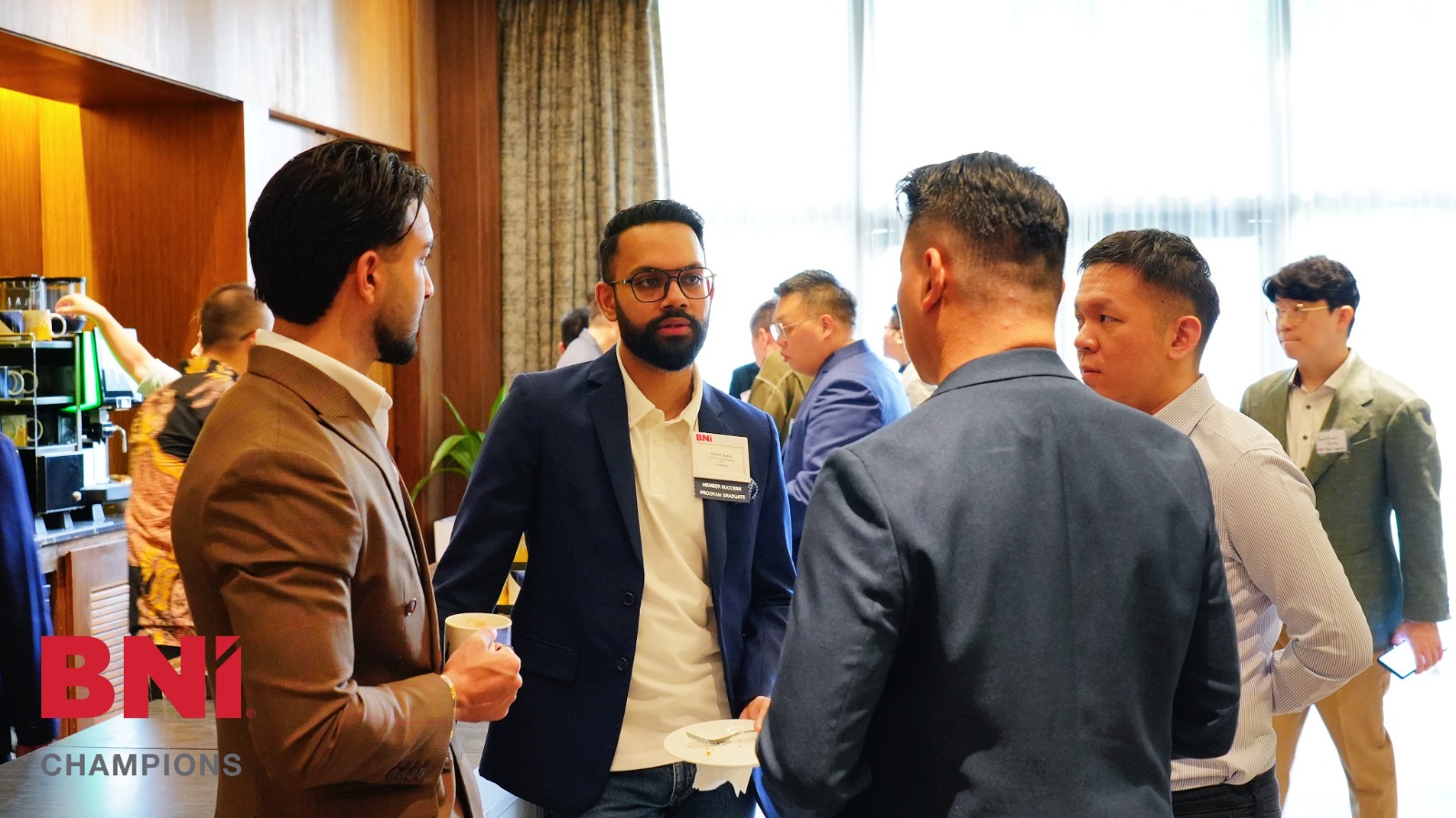 A well-lit room of members networking before the meeting starts