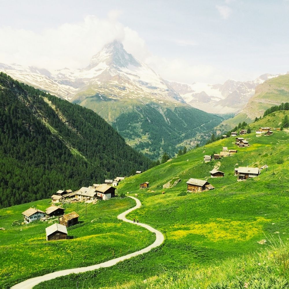 A winding path through an alpine village beneath snow-capped peaks