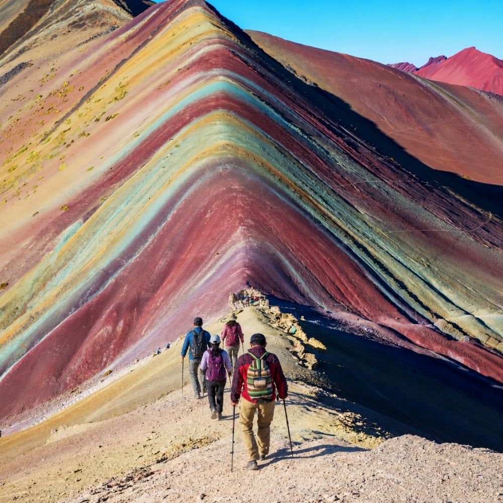 Trekkers walking along a ridge of striped rainbow mountains