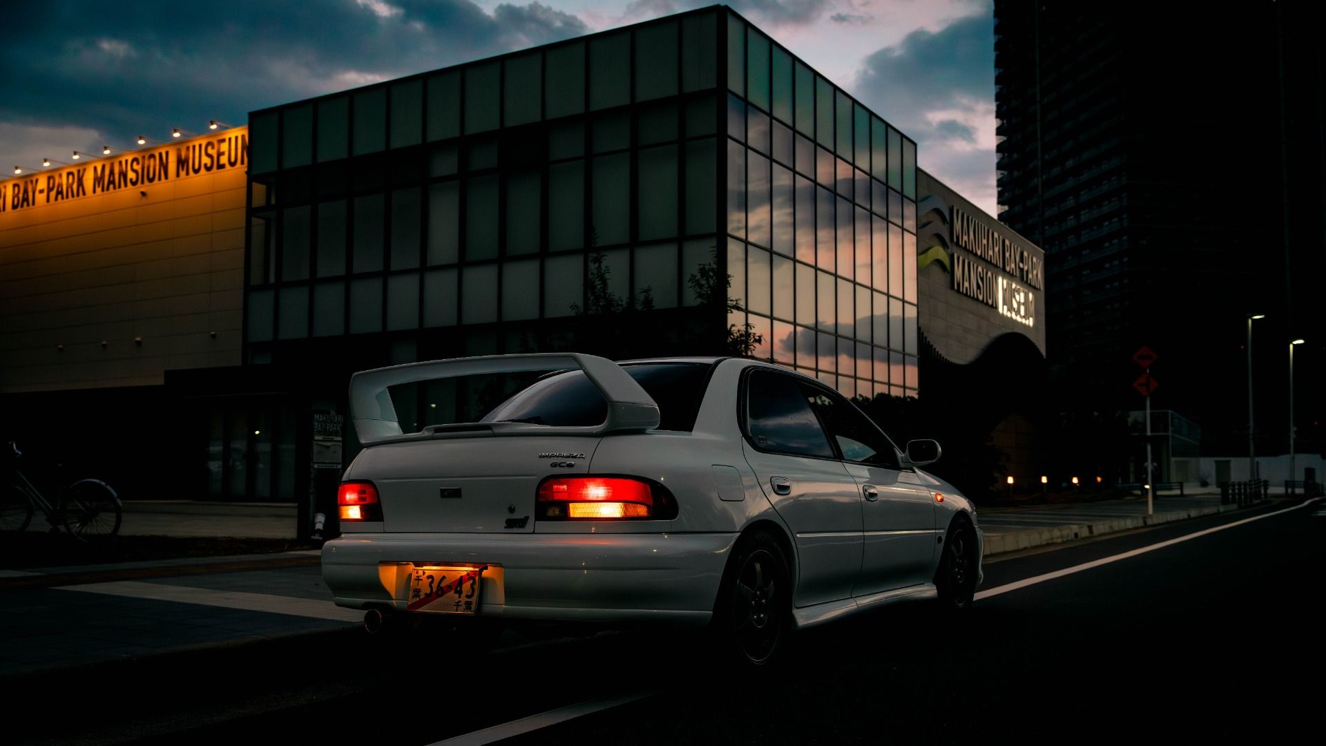 Rear view of a white Subaru Impreza WRX STI at dusk in a city.