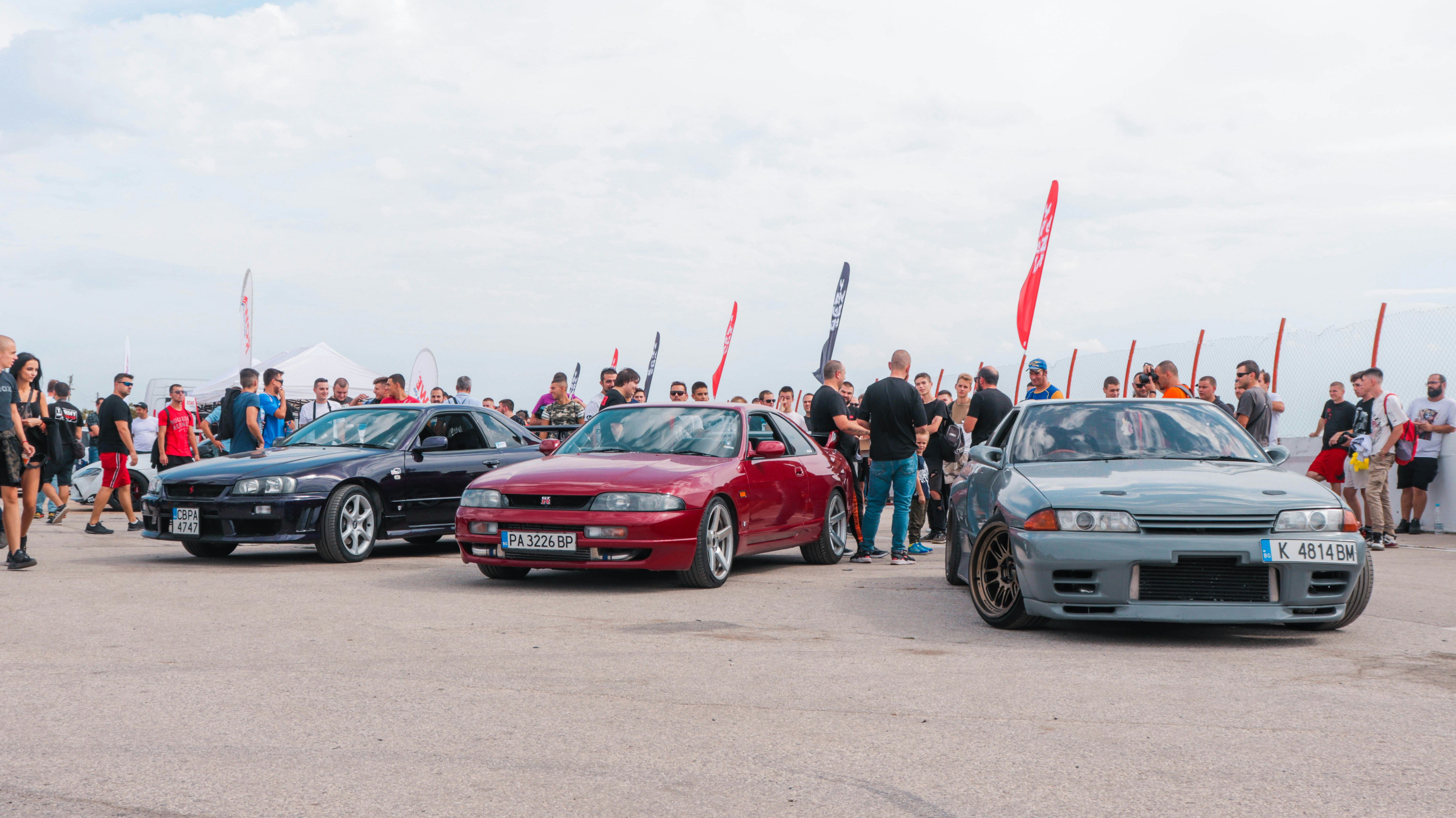 JDM car meet with Nissan Skyline GT-R R32, R33, and R34 models showcased, surrounded by enthusiasts.